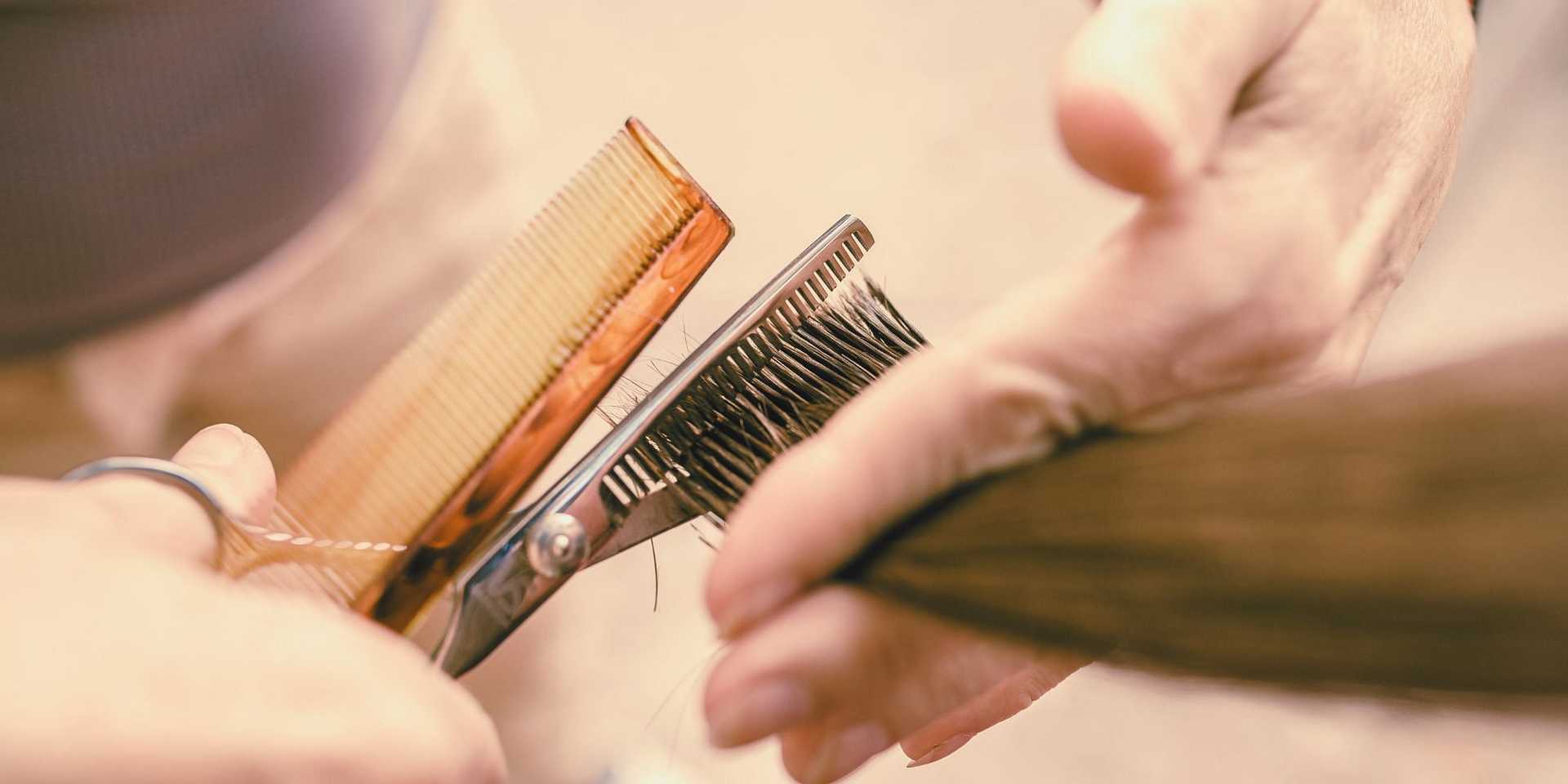 Hairdresser trimming brown hair with scissors and comb.