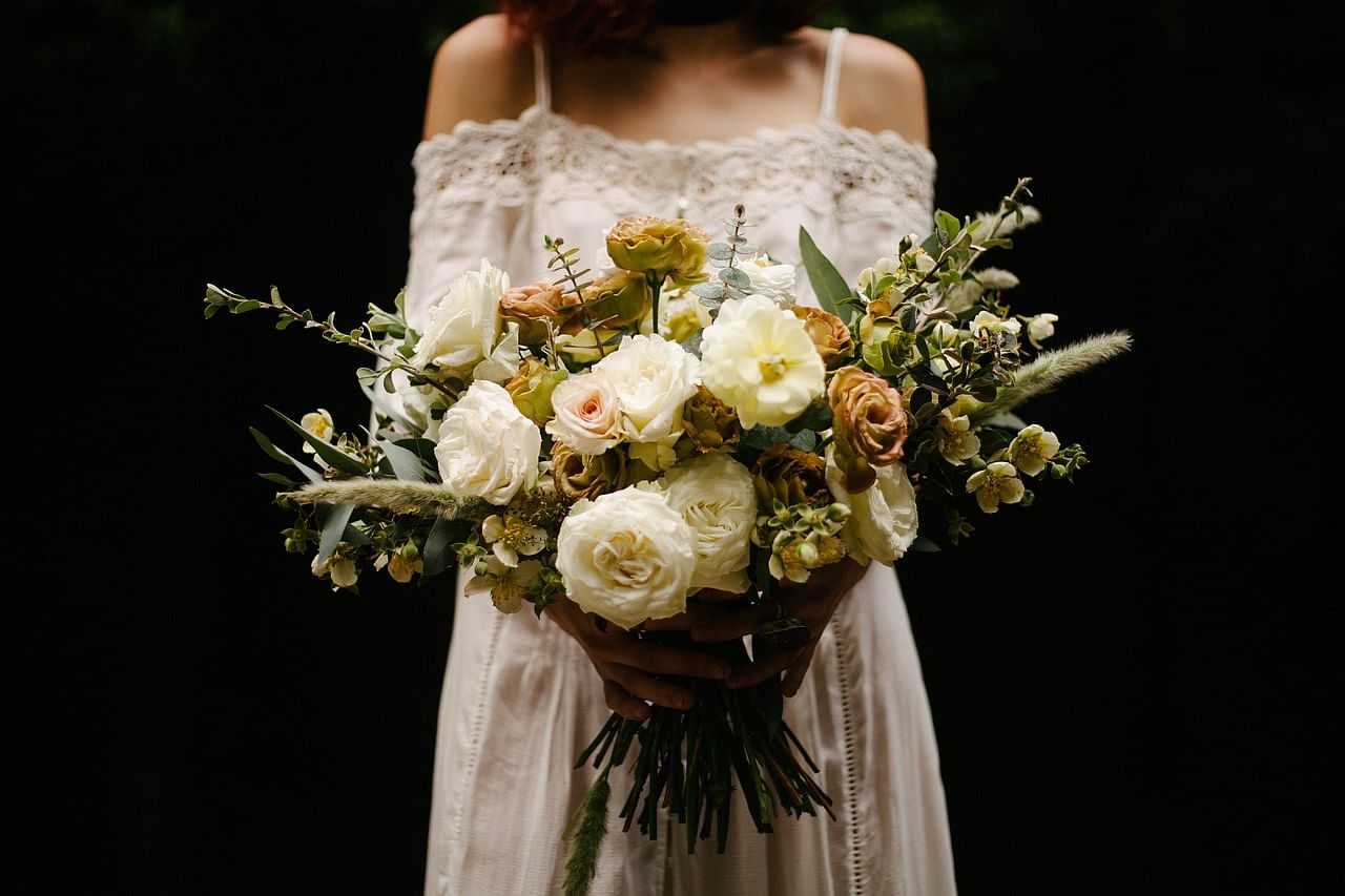 Bride holding a bouquet of white and beige flowers against a dark background.